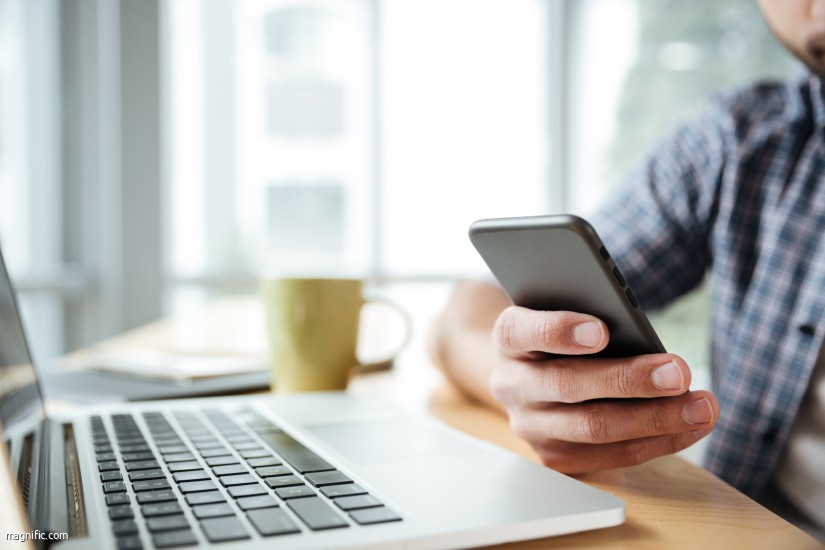 Cropped image of young man sitting in office coworking while using laptop computer and mobile phone.